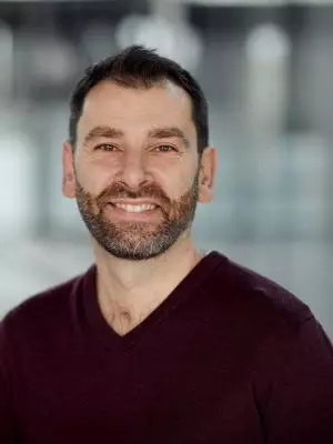 Richard Kemble has short brown hair and a short beard. He is wearing a dark v-neck jumper