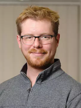 Roan Batten-Powell has short fair hair. He is wearing rectangular glasses and a grey zip-up jumper